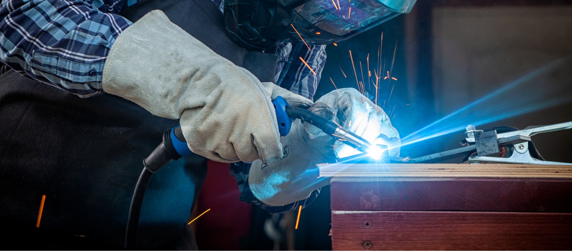 Nahaufnahme einer Person mit Handschuhen, die mit einem Schweißgerät an einem Metallstück arbeitet, sichtbarer Funkenflug